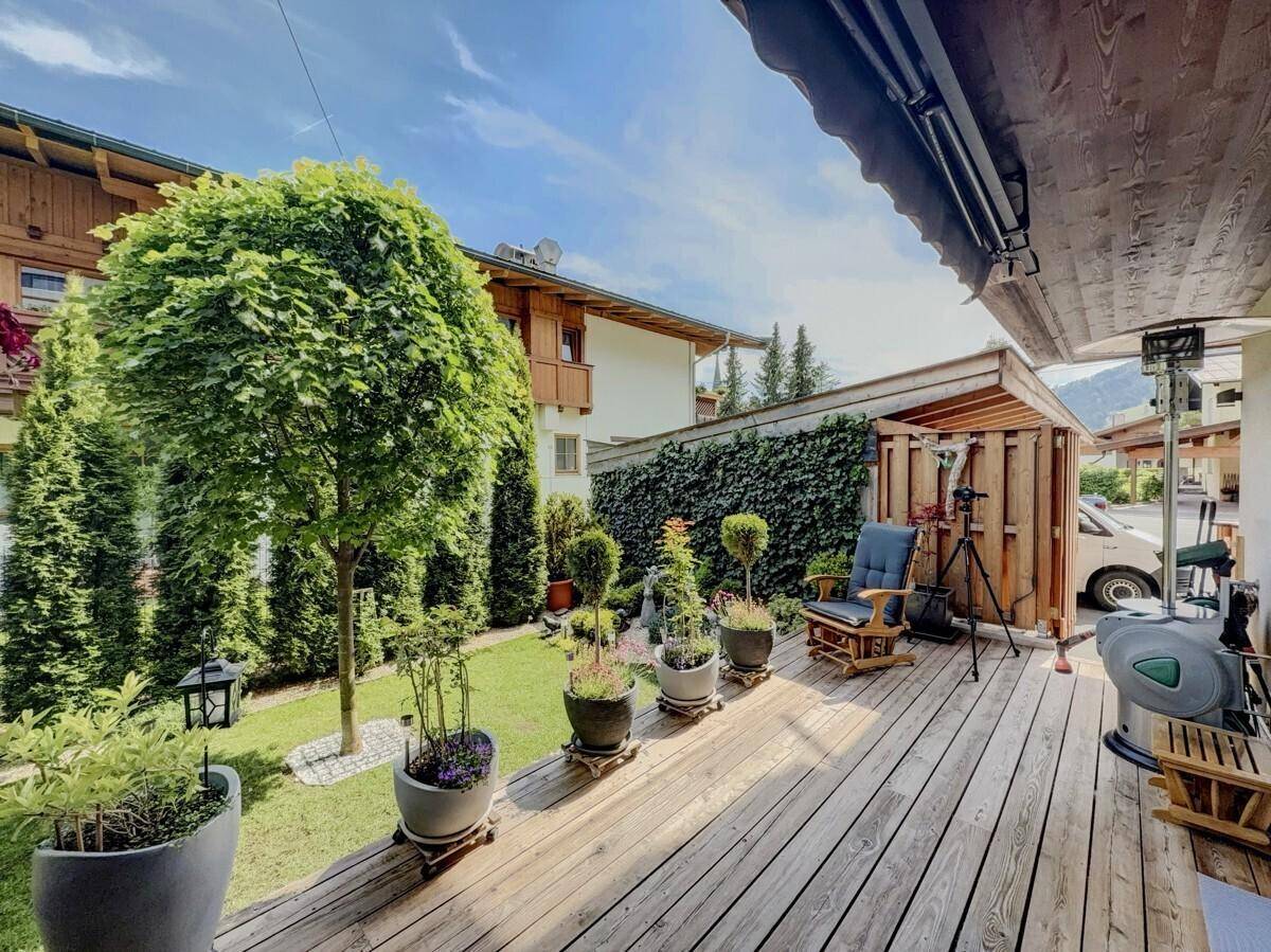 Geräumige Holzterrasse mit Gartenmöbeln, umgeben von einem gepflegten Rasen und Bäumen.