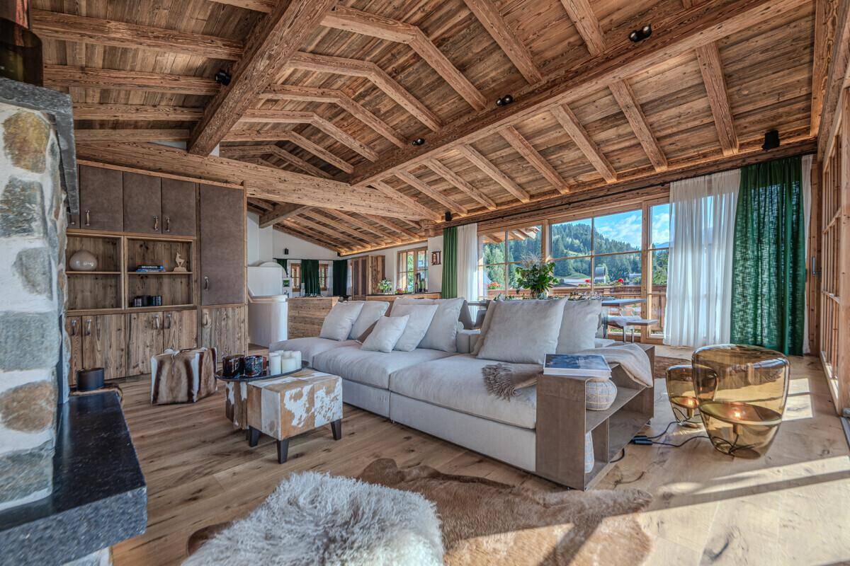 Heller Wohnbereich mit Holzbalkendecke, großem Sofa und Blick auf die umliegende Berglandschaft.