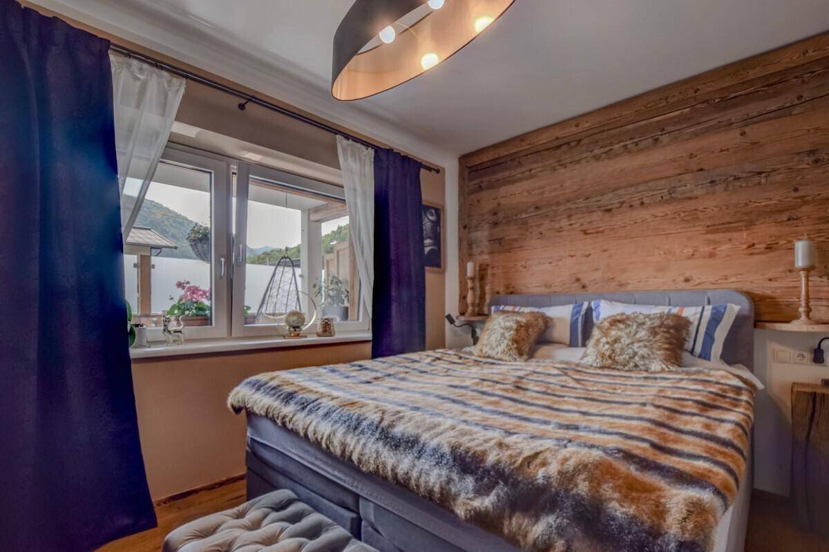 Gemütliches Schlafzimmer im Chalet-Stil mit Holzwand, großem Bett und Blick ins Grüne.