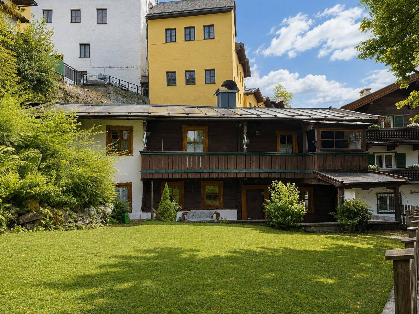 Hinteransicht des Holzhauses mit gepflegtem Rasen und einem Balkon im ersten Stock, umgeben von üppigem Grün.