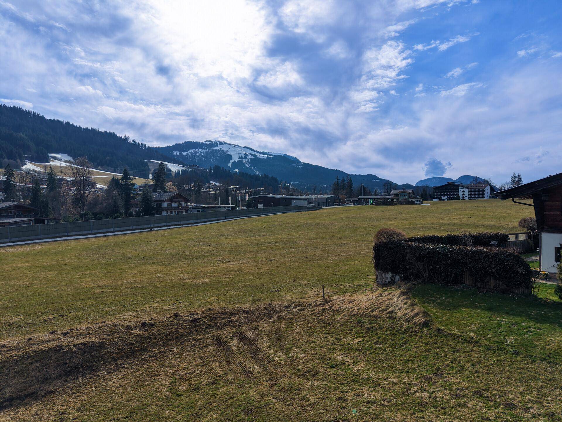 Weitläufige grüne Wiesen mit einem Zaun und schneebedeckten Bergen in der Ferne unter blauem Himmel.