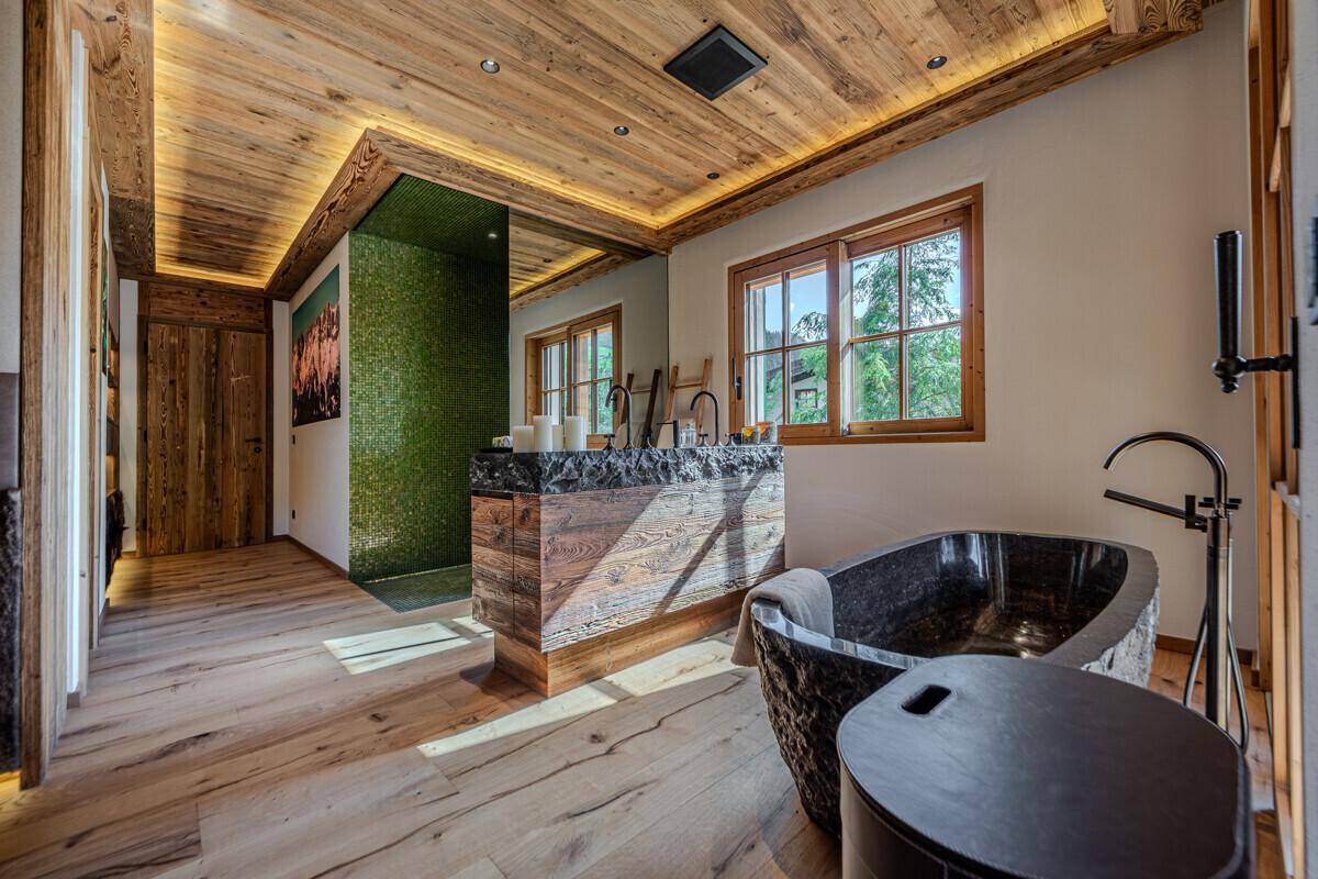 Luxuriöses Badezimmer mit freistehender Steinbadewanne, Holzwaschtisch und indirekter Beleuchtung.