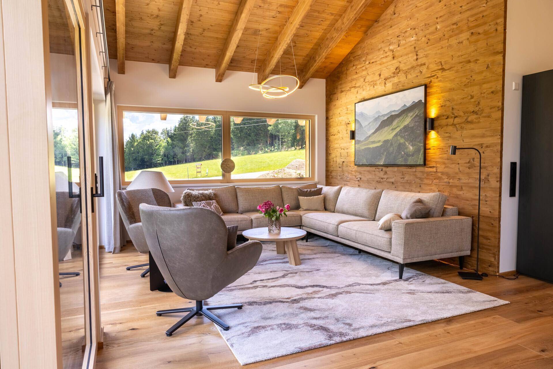 Helles Wohnzimmer mit Holzbalkendecke, bequemen Sofas und Bergblick durch große Fenster.