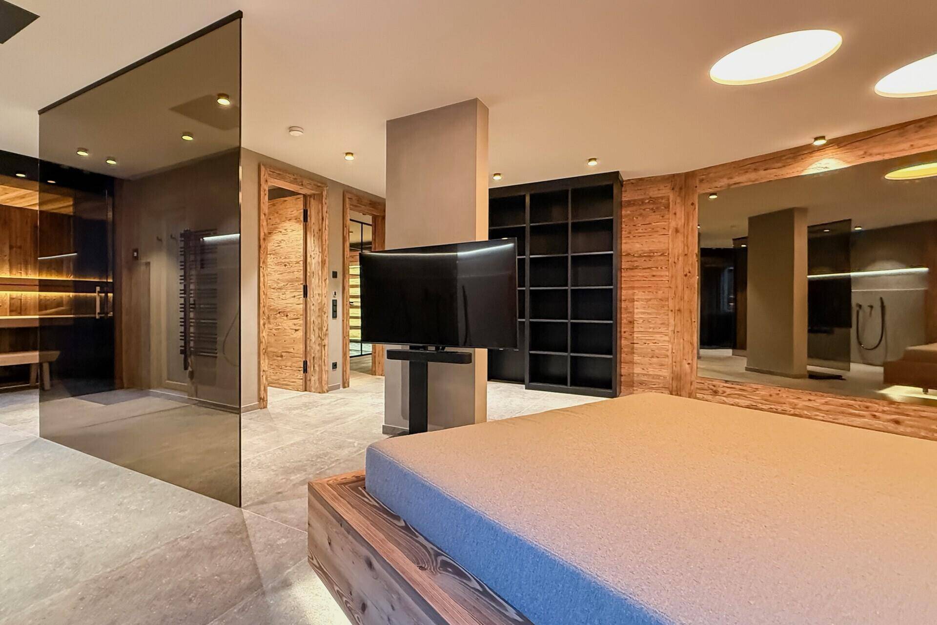 Schlafzimmer mit Holzbett, Fernseher und großem Spiegel, modern und funktional eingerichtet.
