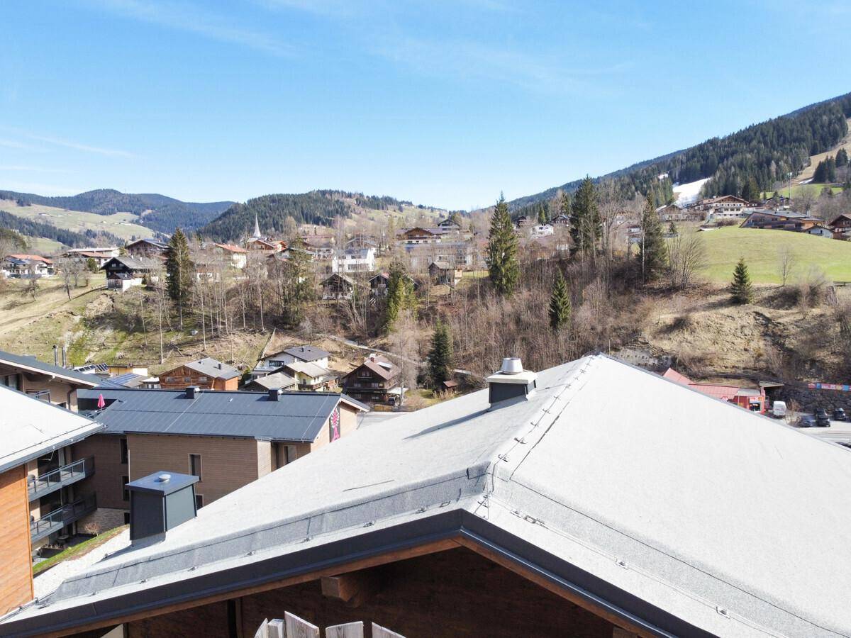 Blick über die Dächer der umliegenden Gebäude und die weite Berglandschaft unter blauem Himmel.