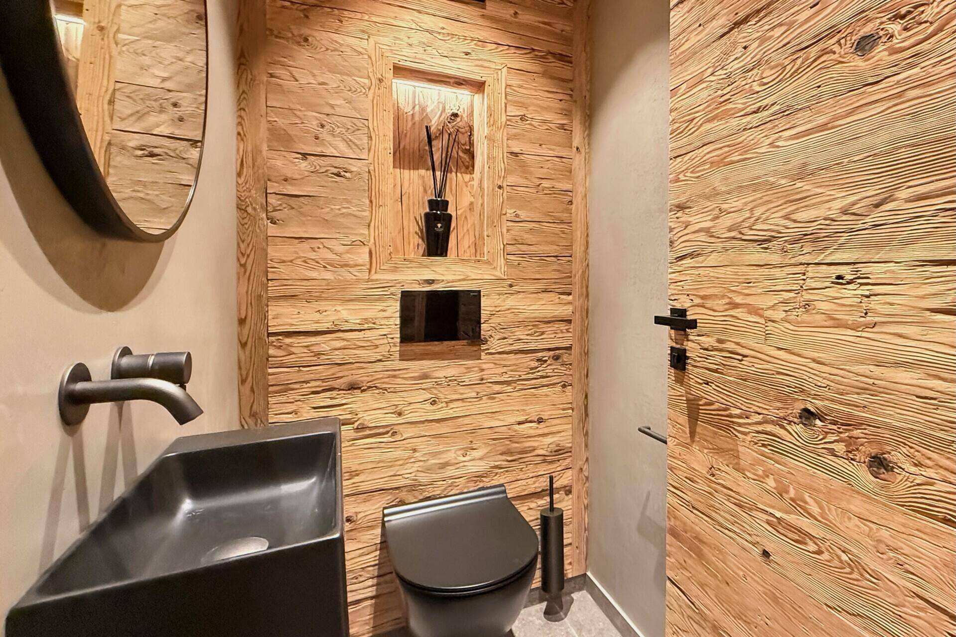 Stilvolles Gäste-WC mit Holzwänden, beleuchtetem Spiegel und modernem Waschbecken.