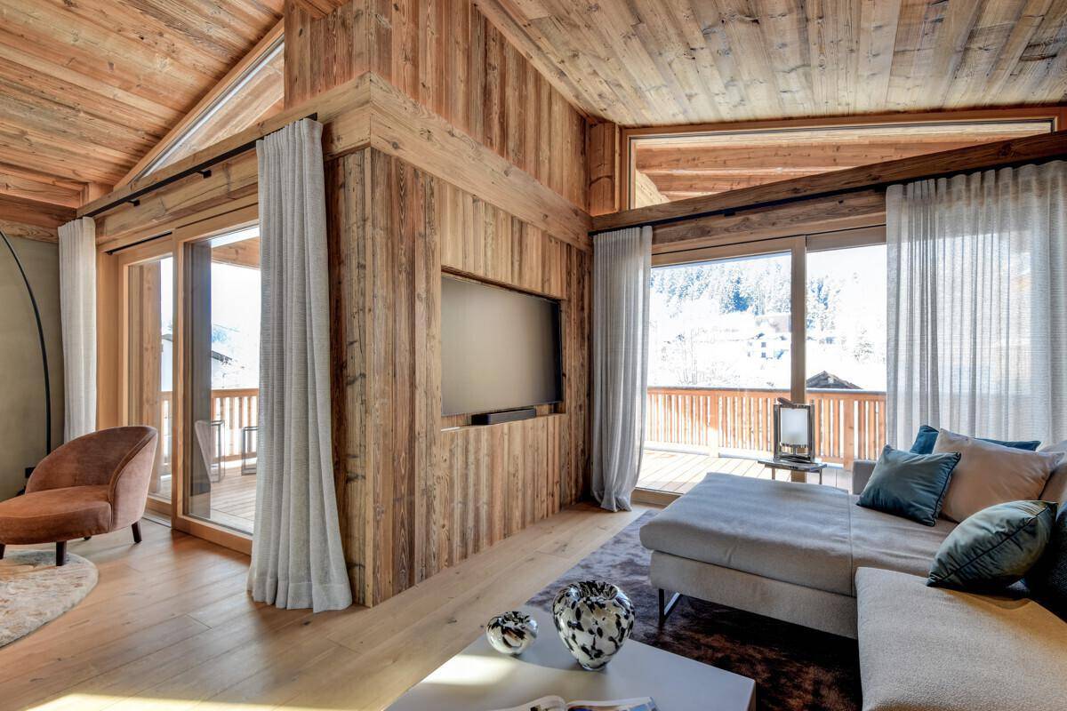 Gemütliches Wohnzimmer mit großem Sofa, Holzwänden und Blick auf die verschneite Landschaft.