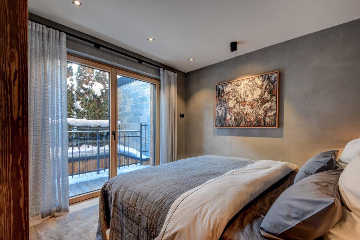 Modernes Schlafzimmer mit Holzwand, großem Bett und Zugang zu einem kleinen Balkon mit Winterblick.