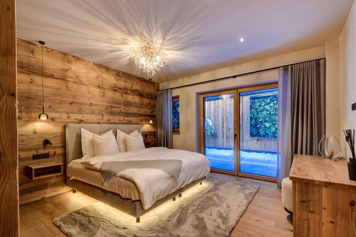 Helles Schlafzimmer mit Holzwand, großem Bett und Zugang zum Außenbereich.