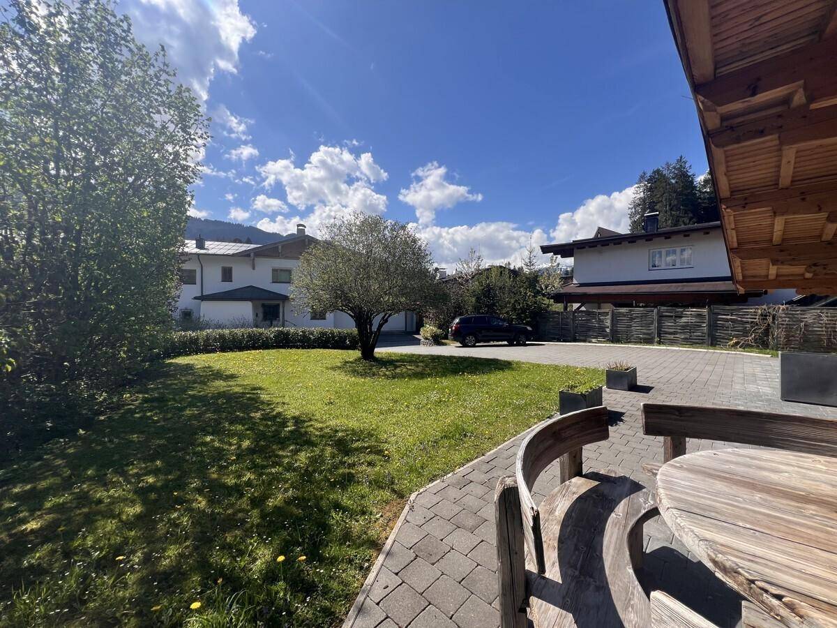 Grüner Gartenbereich mit Bäumen und einer gepflasterten Auffahrt vor dem Haus.