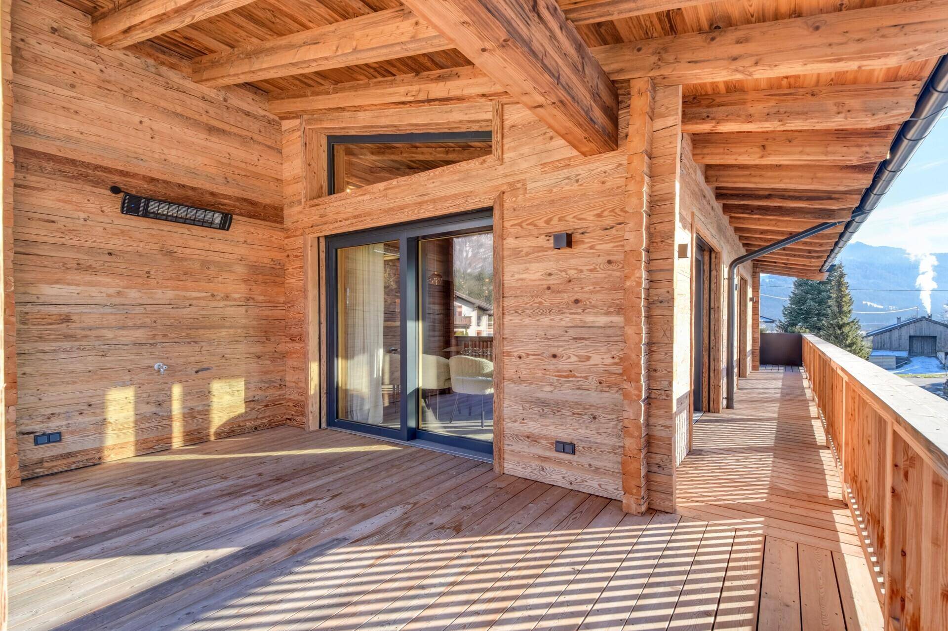 Langer Holzbalkon mit Schiebetüren und Bergblick, perfekt für Outdoor-Living und Entspannung.