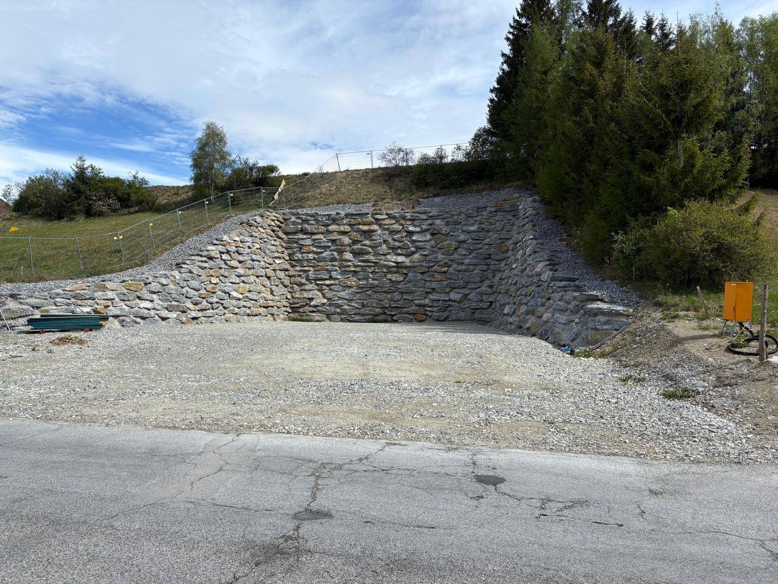 Eine imposante Natursteinmauer mit Schotterfläche davor und einer angrenzenden Straße.