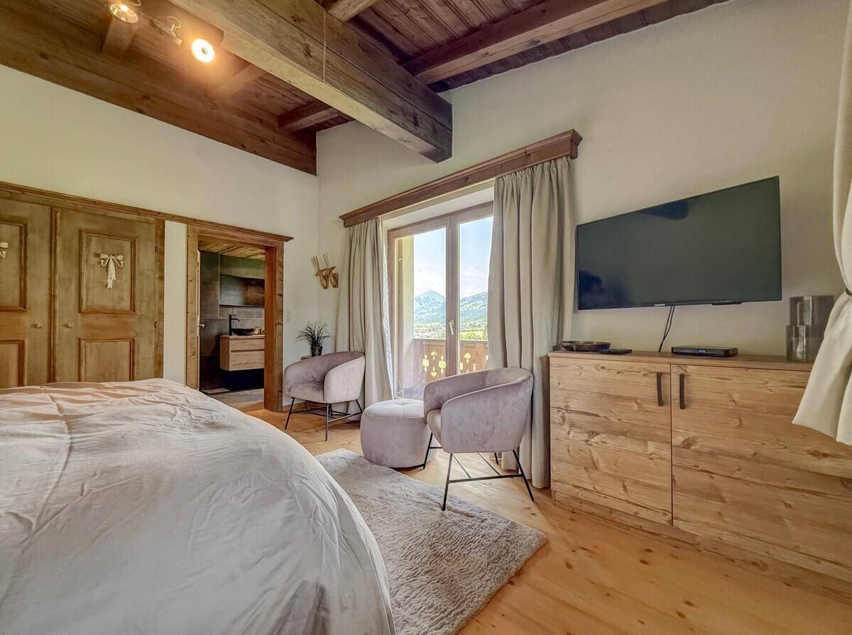 Schlafzimmer mit Holzbalkendecke, Doppelbett und Balkonzugang mit Bergblick.