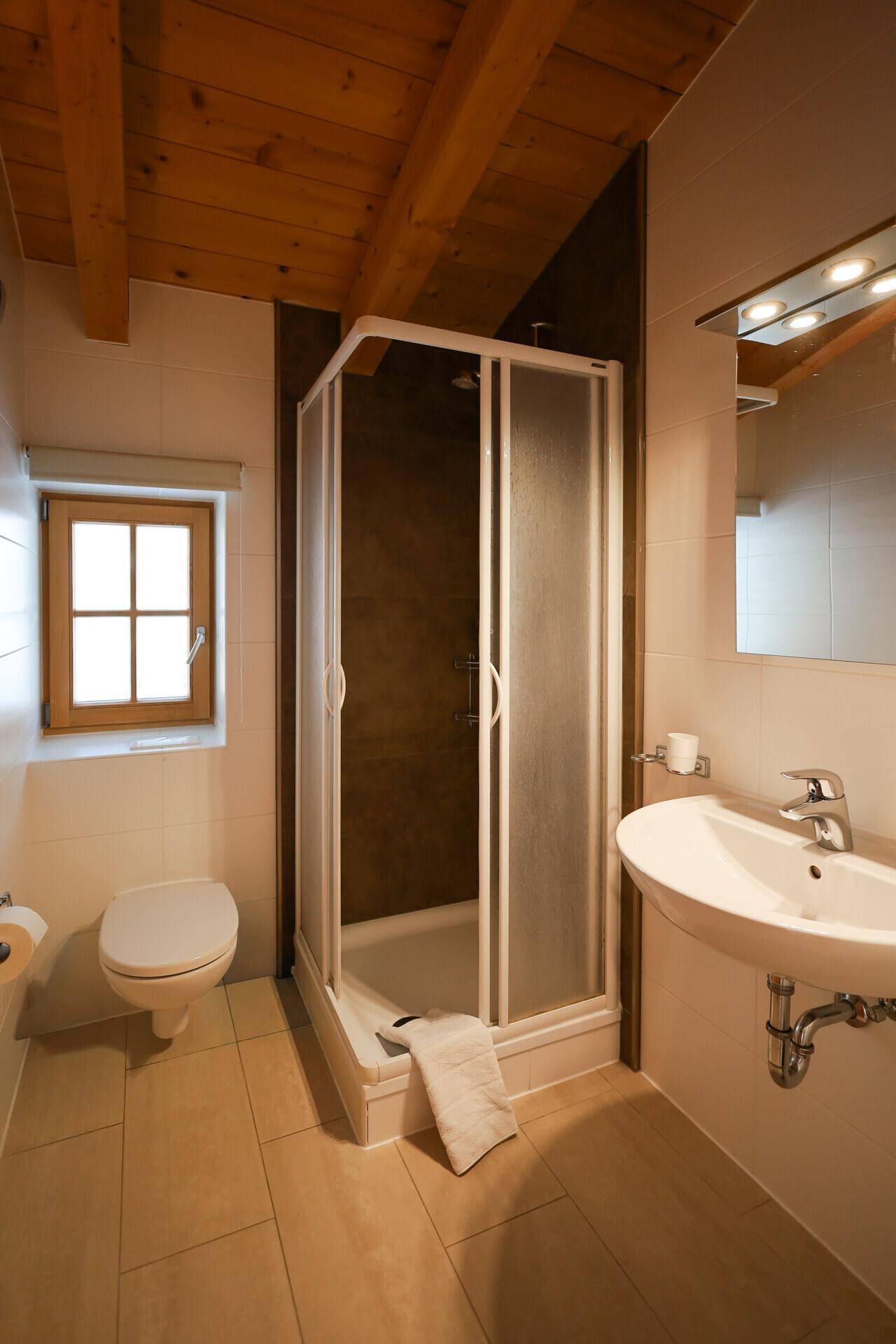 Helles Badezimmer mit Duschkabine, Waschbecken und Fenster für Tageslicht.