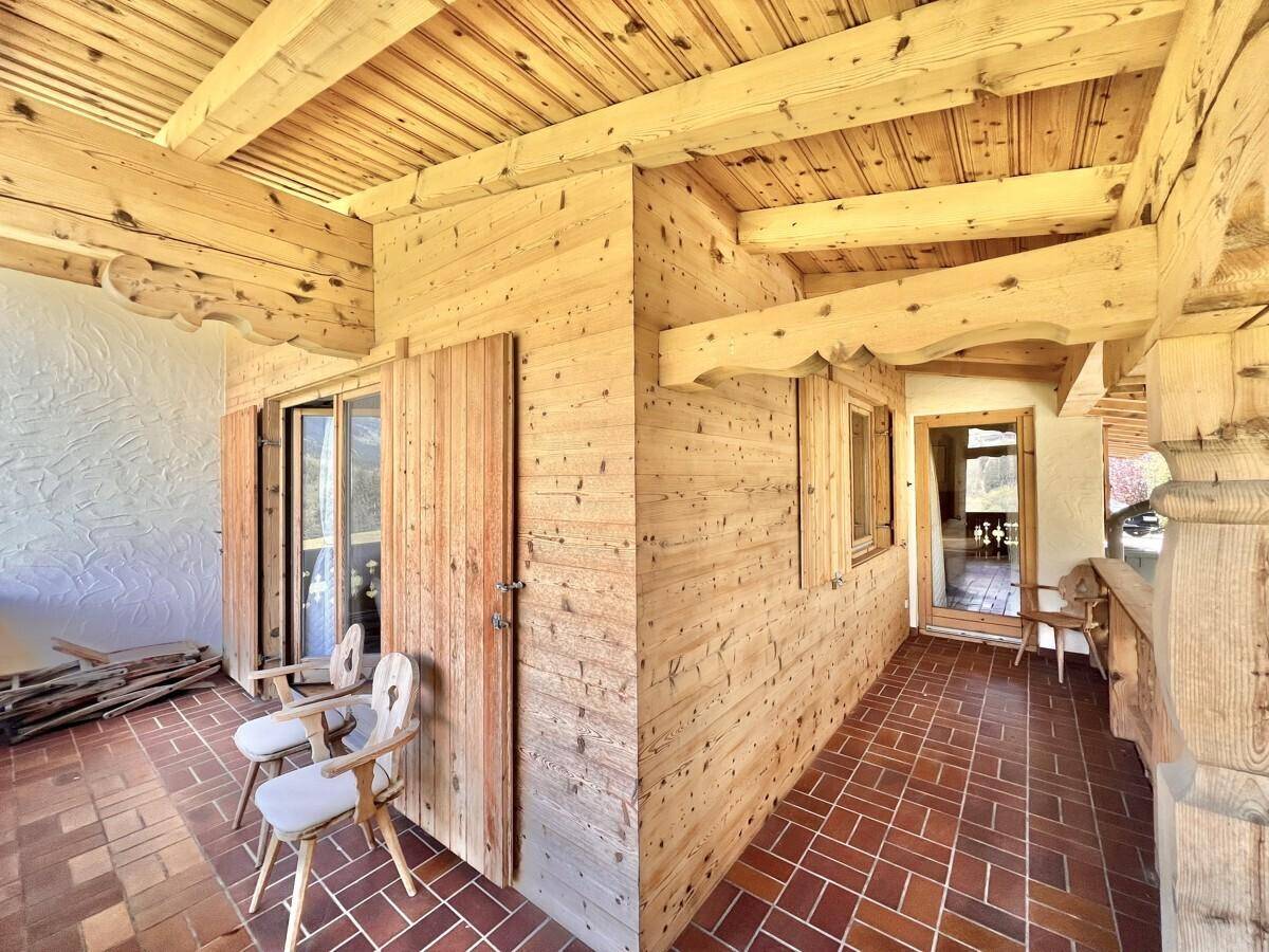 Überdachte Holzloggia mit Fliesenboden und traditionellen Holzmöbeln, ideal zum Entspannen.