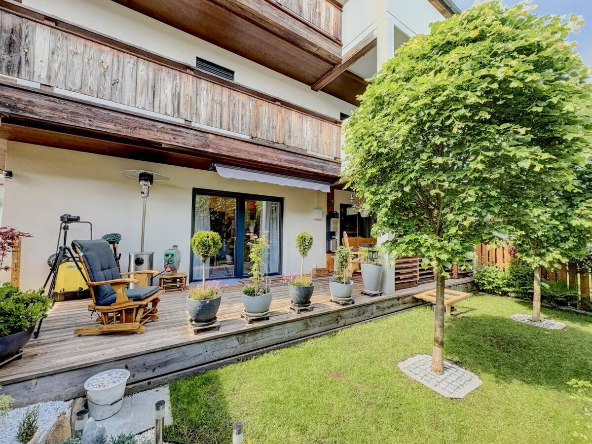 Geräumige Holzterrasse mit Gartenmöbeln, umgeben von einem gepflegten Rasen und Bäumen.