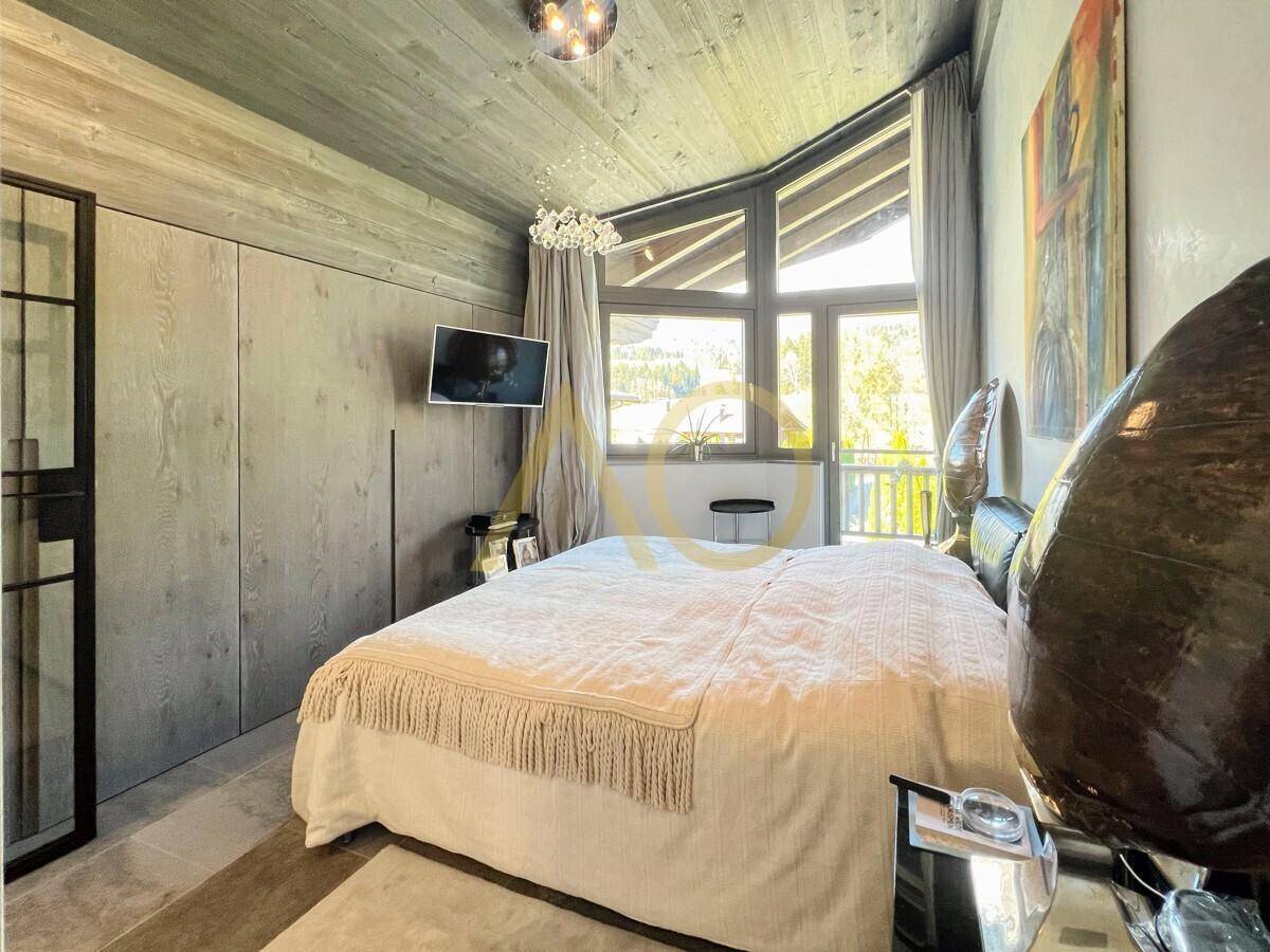 Helles Schlafzimmer mit Holzbalkendecke, großen Fenstern und Blick ins Grüne.