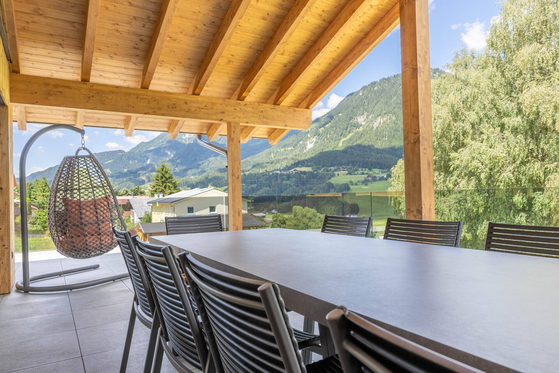 Überdachte Terrasse mit Esstisch, Hängesessel und weitem Blick auf die Berge.