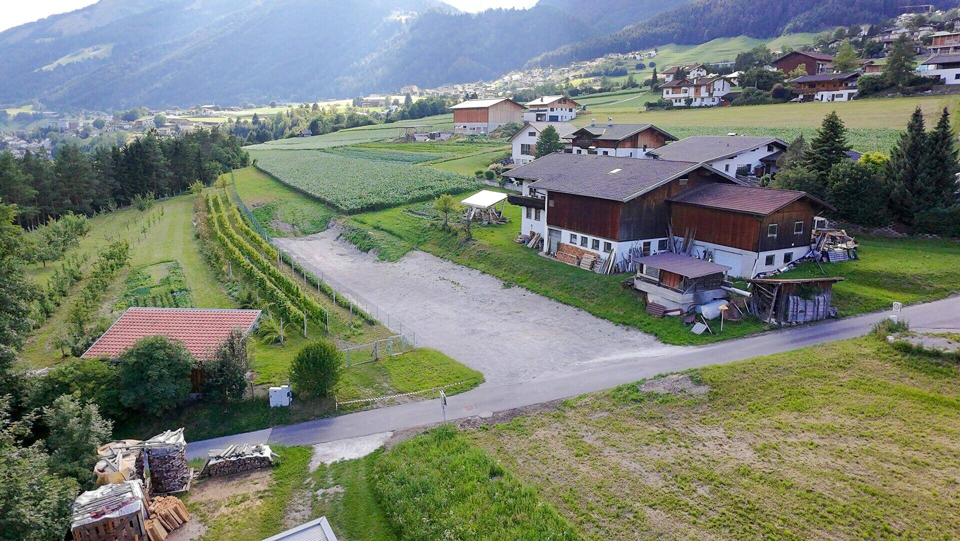 Luftaufnahme einer ländlichen Gegend mit Wohnhäusern, Feldern, Weinbergen und einer Zufahrtsstraße.