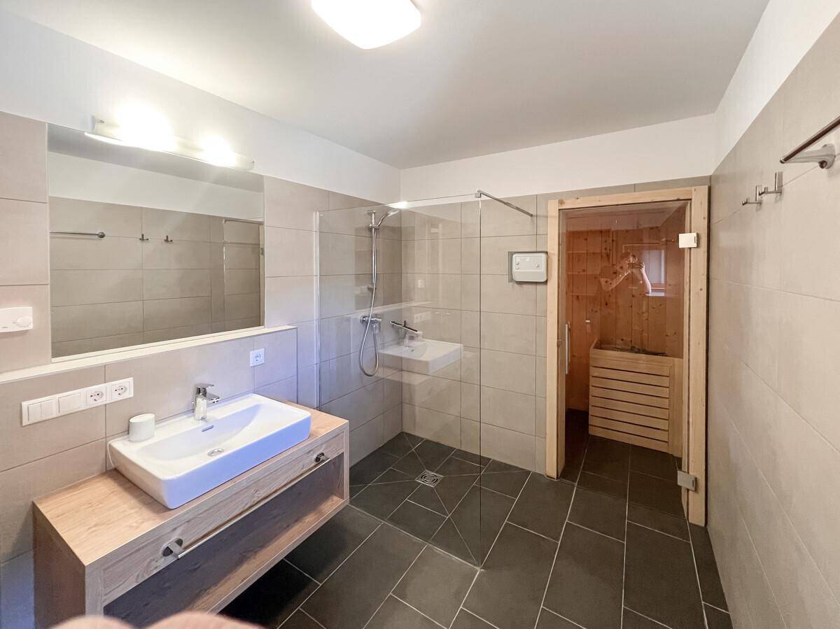 Modernes Badezimmer mit Dusche, Einzelwaschbecken und direktem Zugang zu einer privaten Sauna.