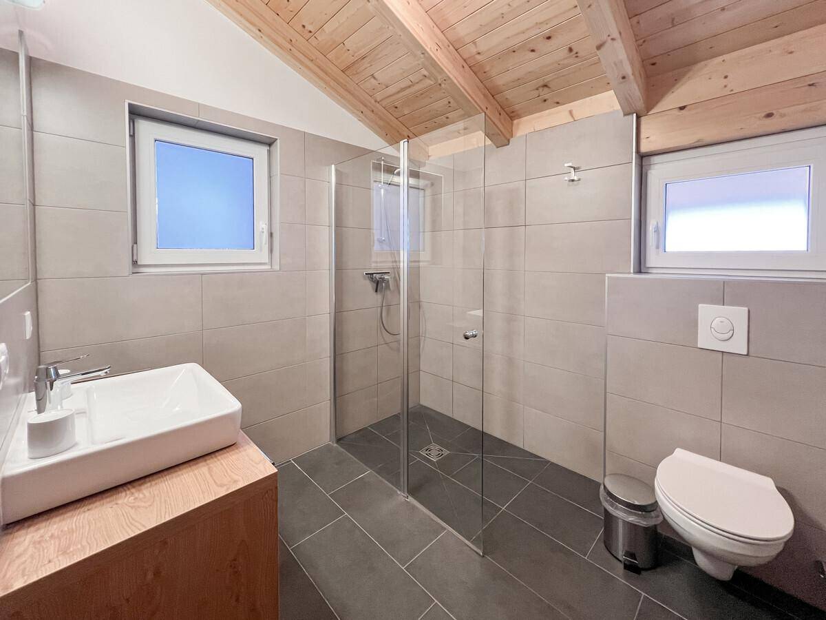 Modernes Badezimmer mit Dusche, Einzelwaschbecken und zwei Fenstern für natürliches Licht.