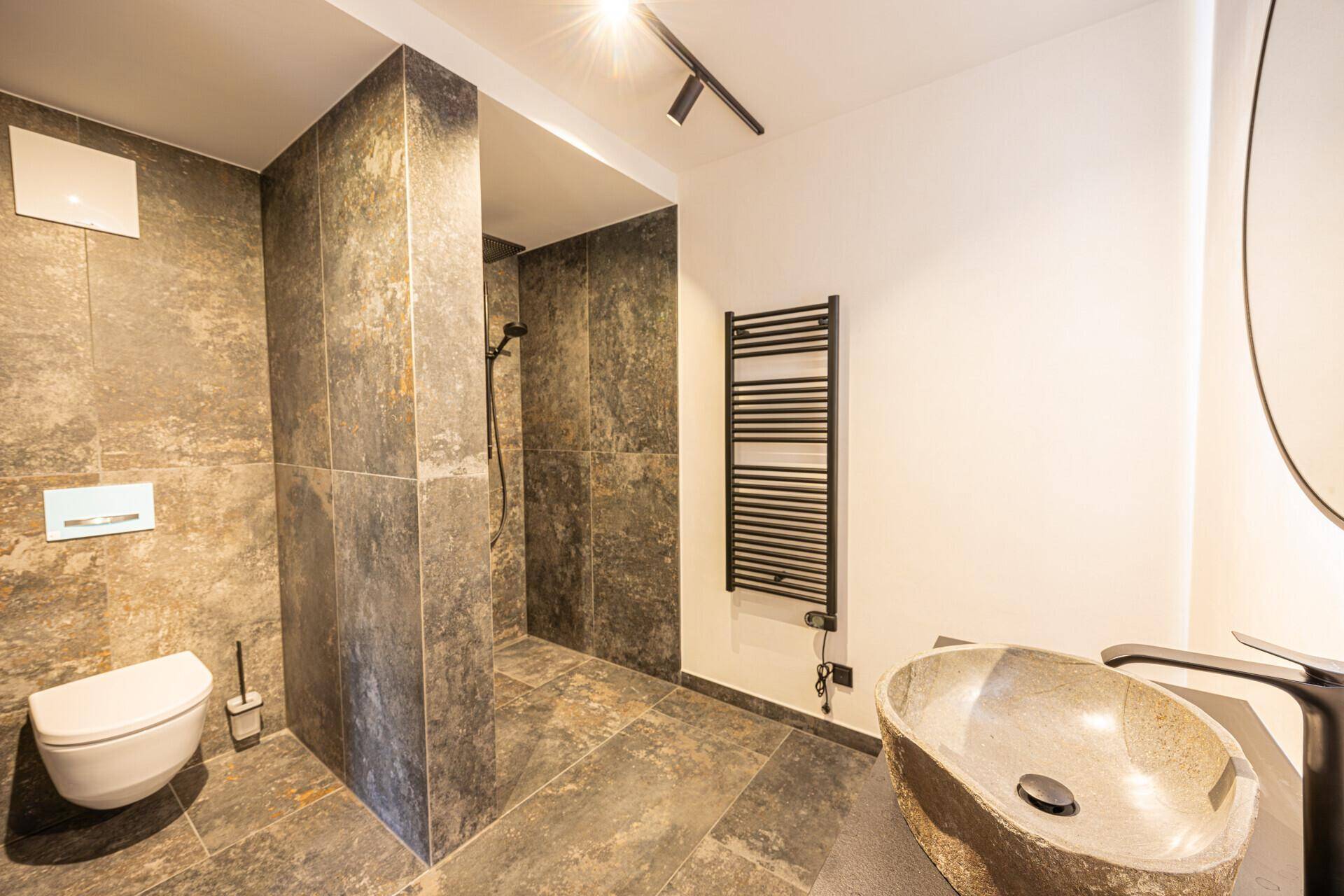 Modernes Badezimmer mit begehbarer Dusche, Wand-WC und Natursteinwaschbecken.