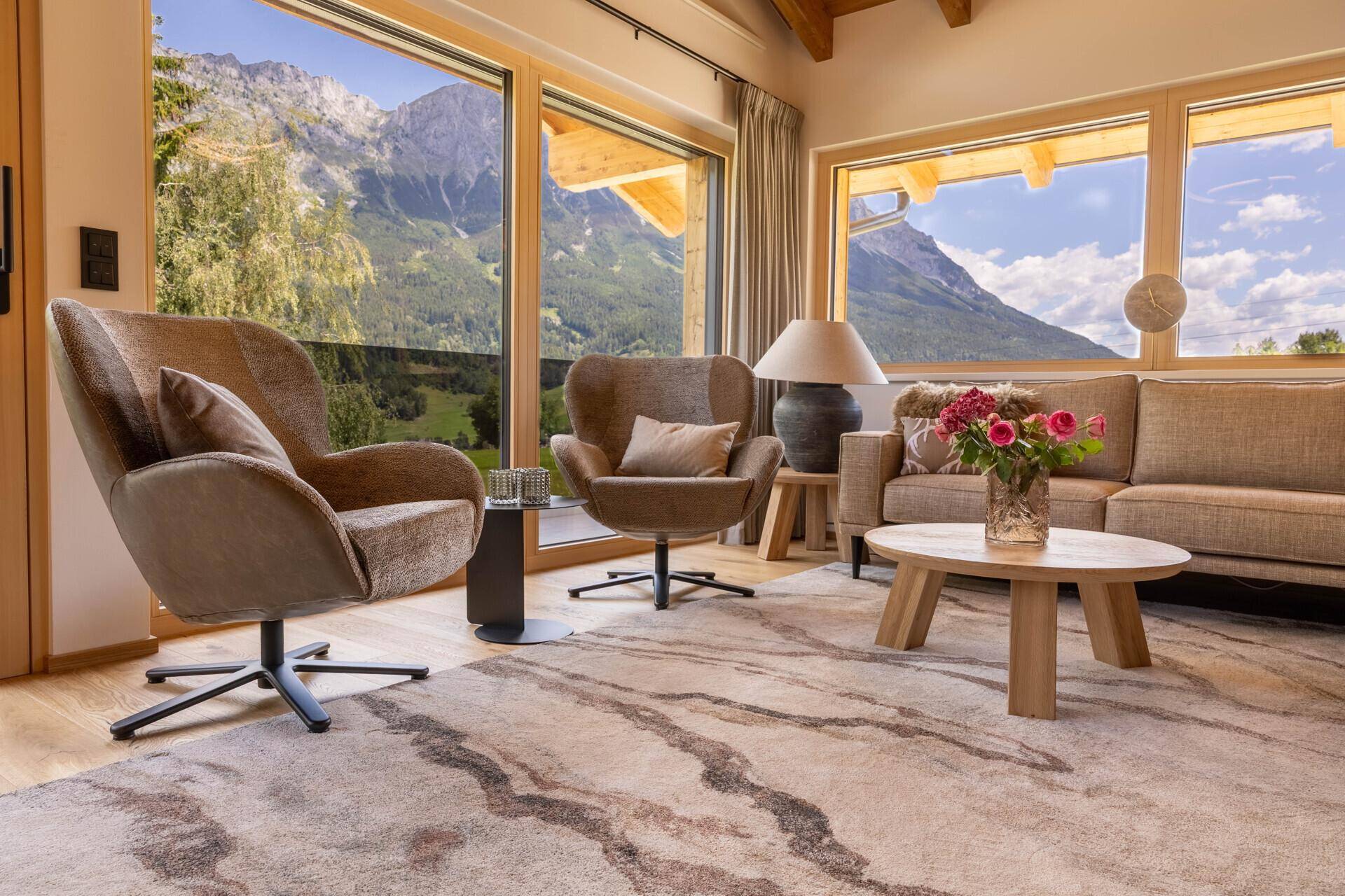 Gemütliches Wohnzimmer mit beigen Möbeln, Holzboden und Panoramablick auf die Berge.