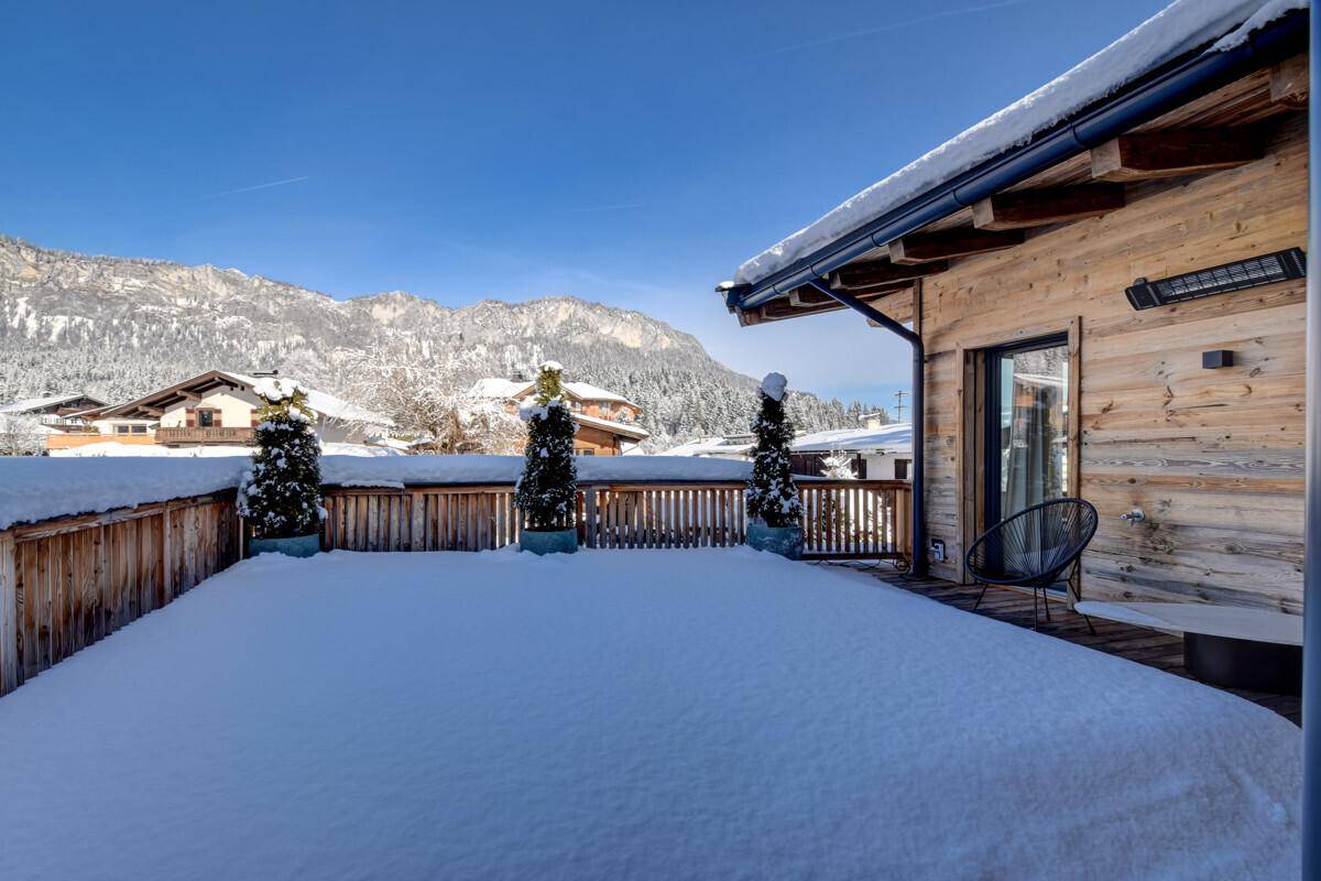 Weitläufige Terrasse mit Holzboden, Schneedecke und Blick auf die Berglandschaft.