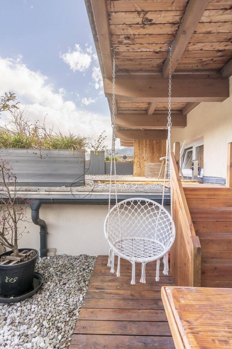 Gemütlicher Hängesessel auf der Holzterrasse, umgeben von Kies und Pflanzen.
