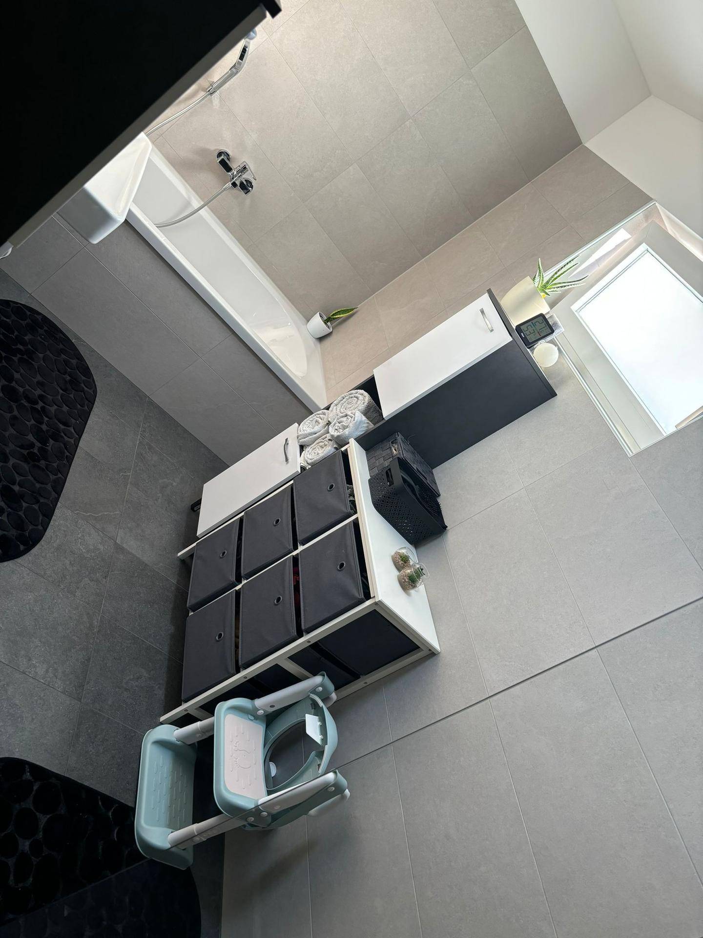 Helles Badezimmer mit Badewanne, Fenster und praktischen Aufbewahrungsmöbeln.