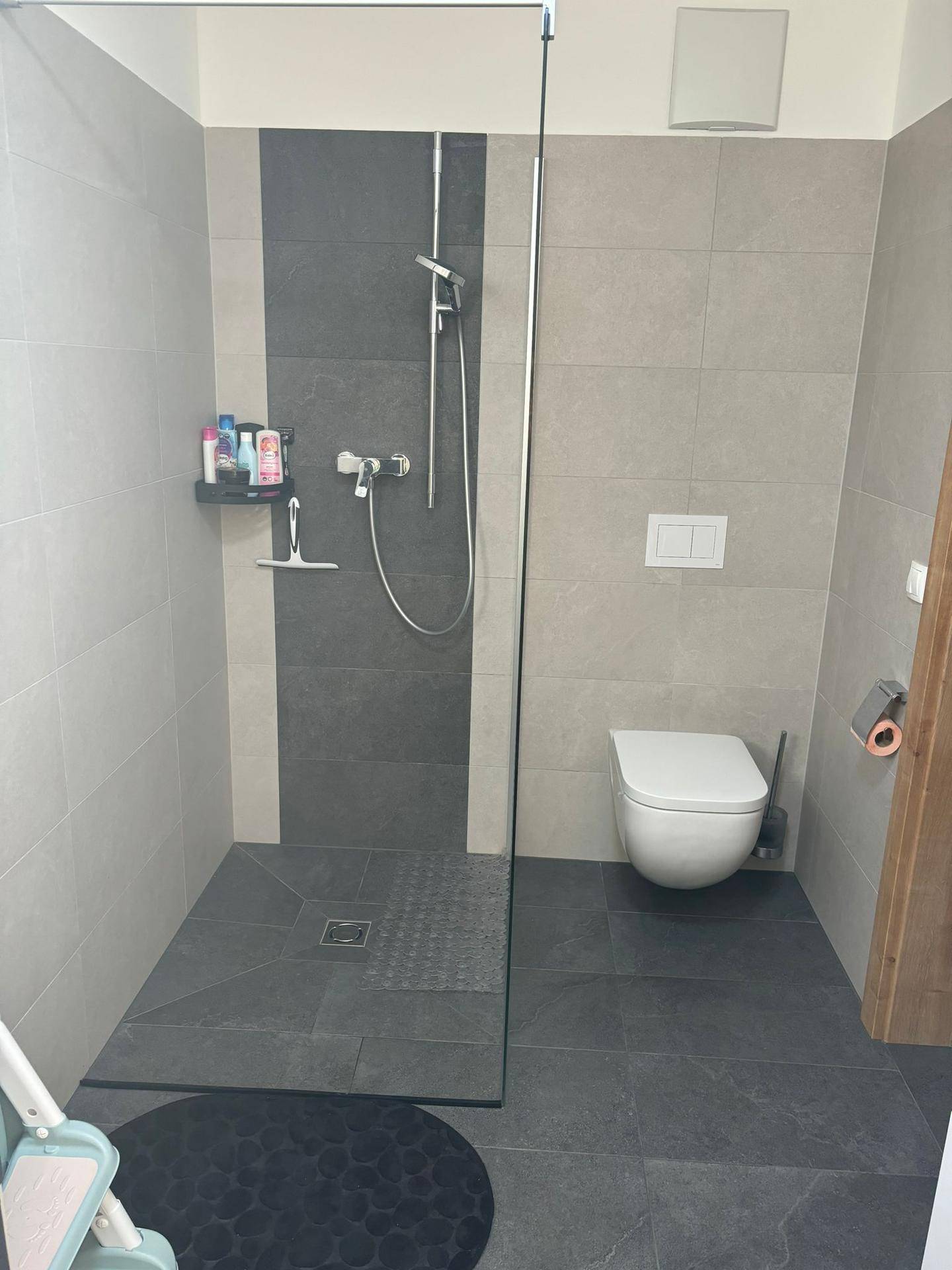 Modernes Badezimmer mit ebenerdiger Dusche, Wand-WC und grauen Fliesen.