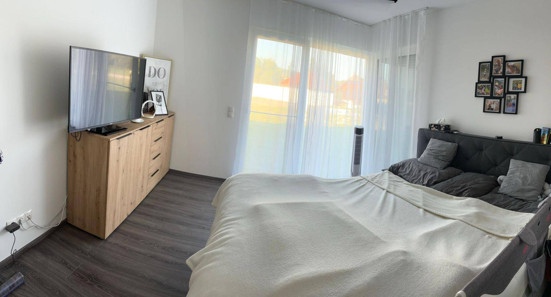 Schlafzimmer mit Doppelbett, Kommode und großen Fenstern für viel Tageslicht.