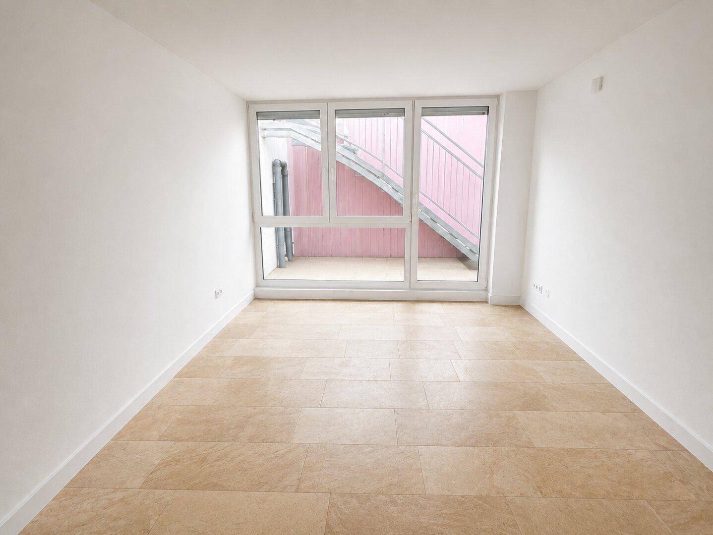 Helles Zimmer mit großem Fenster und Blick auf die Außentreppe, ideal als Schlaf- oder Gästezimmer.