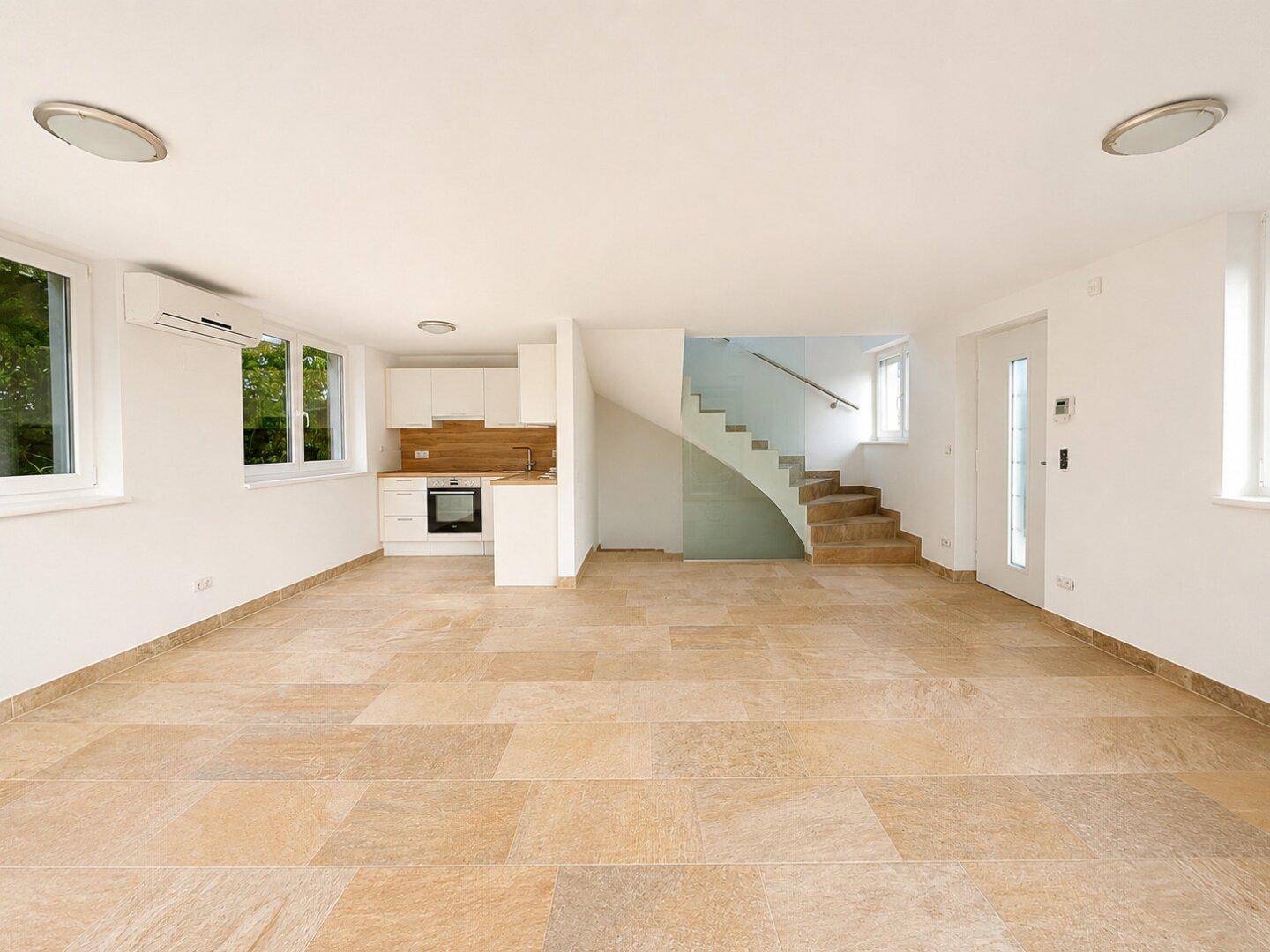 Offener Wohnbereich mit integrierter Küchenzeile und moderner Treppe mit Glasgeländer.