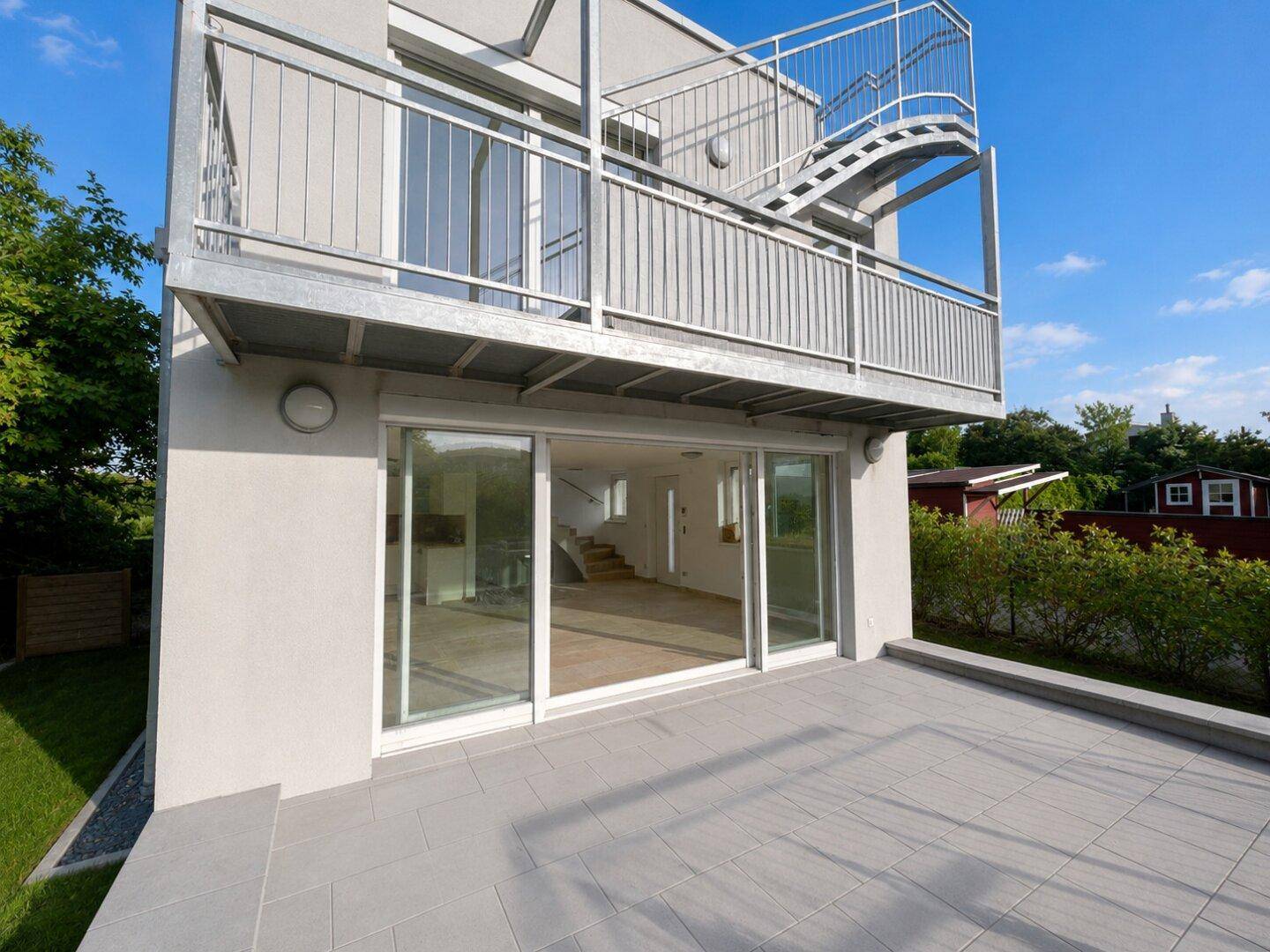 Moderne Gebäudefassade mit großer Terrasse im Erdgeschoss und Balkon mit Außentreppe.