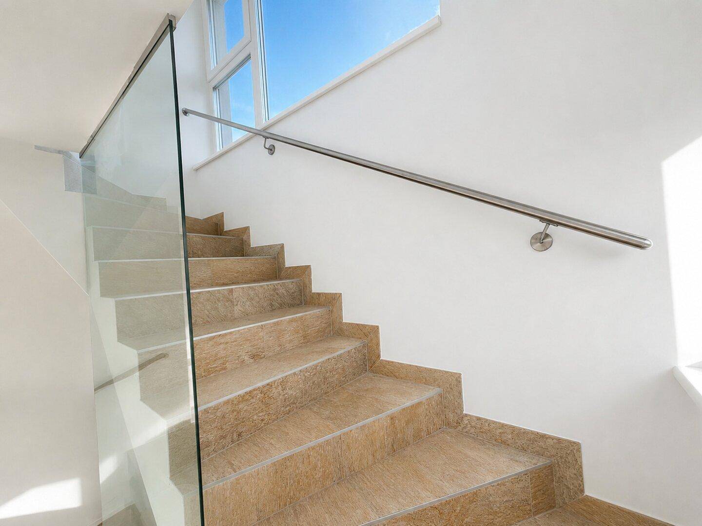 Moderne Treppe mit Fliesenstufen, Glasgeländer und einem eleganten Edelstahlhandlauf.
