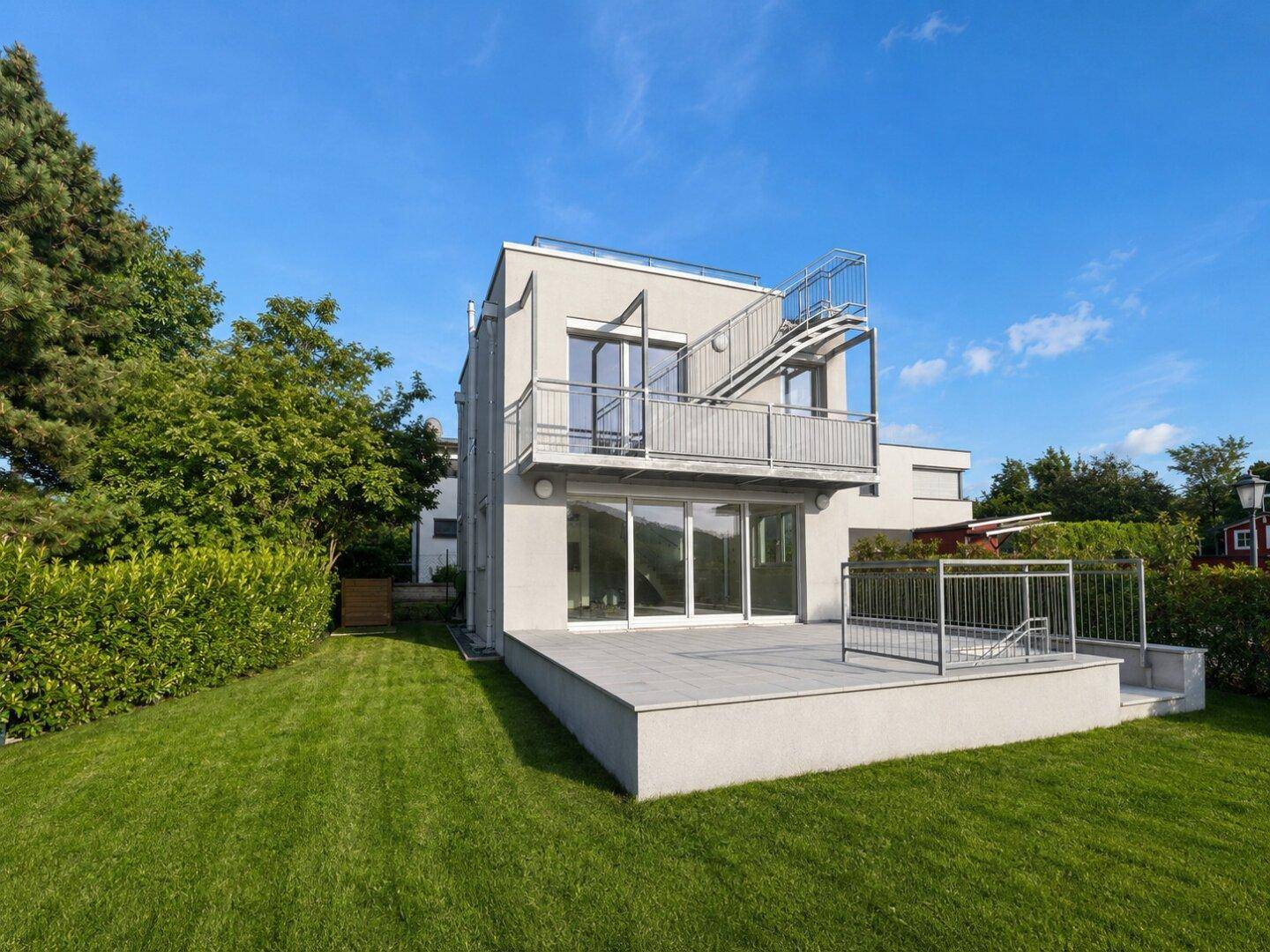 Ansicht des modernen Hauses vom Garten aus, mit Terrasse, Balkon und weitläufiger Rasenfläche.