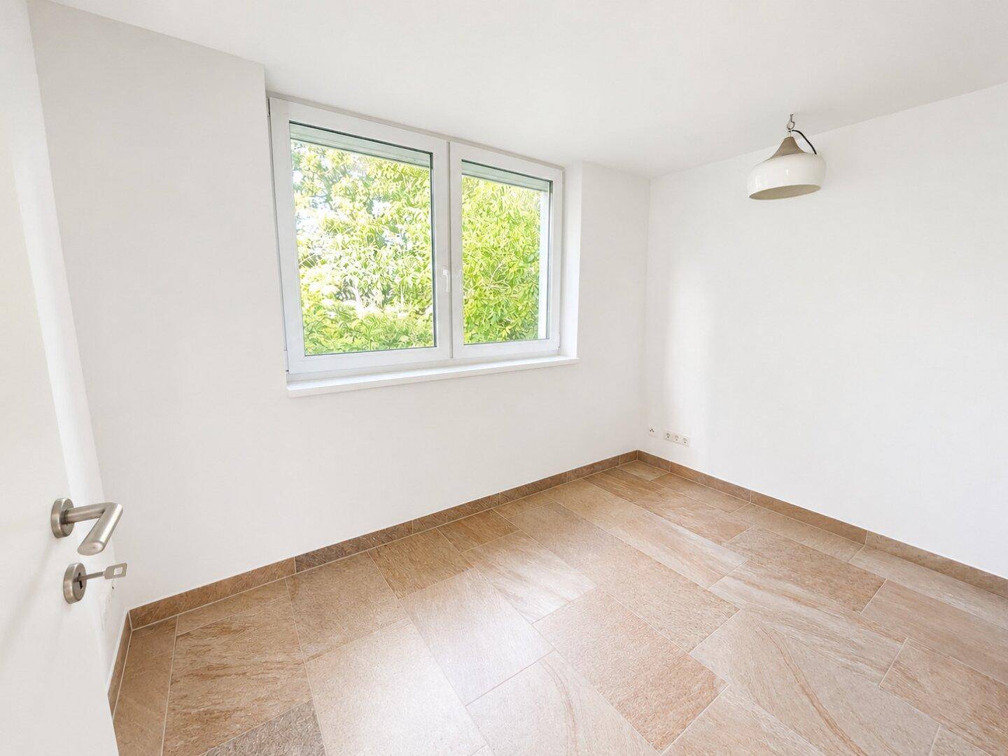 Helles Schlafzimmer mit Fliesenboden und einem Fenster, das viel Tageslicht hereinlässt.