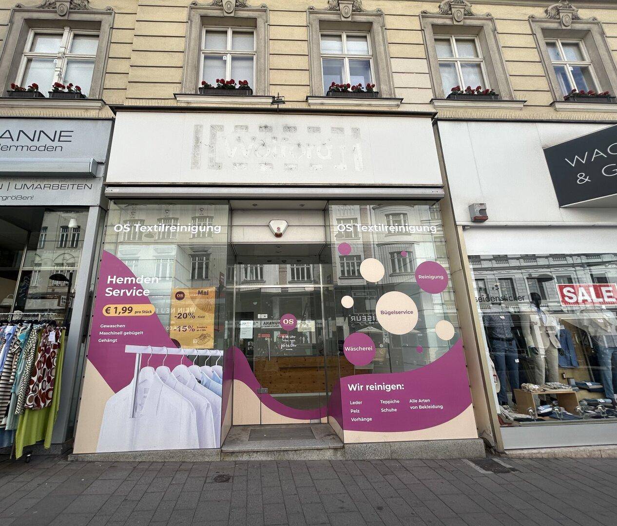 Fassade eines Geschäftsgebäudes mit großen Schaufenstern und Werbung für eine Textilreinigung in der Stadt.