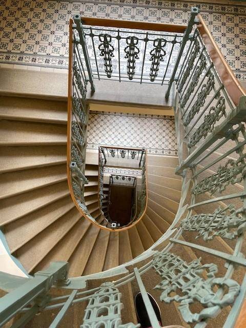 Blick von oben auf ein elegantes Wendeltreppenhaus mit gemusterten Fliesen und schmiedeeisernem Geländer.