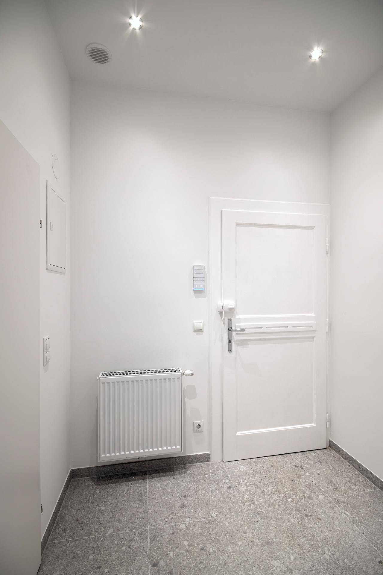 Heller Eingangsbereich mit grauen Fliesen, einer weißen Tür und einem Heizkörper, modern und funktional.