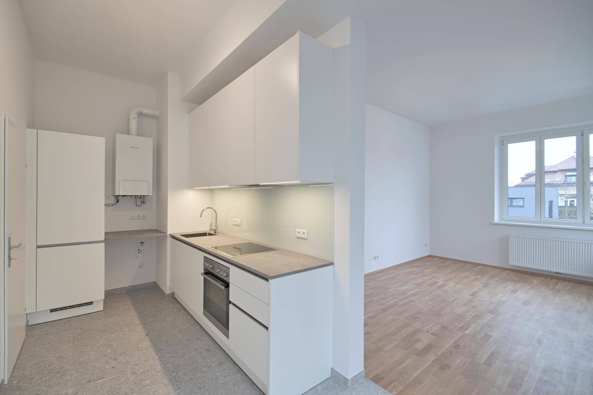Moderne Küchenzeile mit weißen Schränken und integrierten Geräten, offen zu einem Raum mit Holzfußboden.