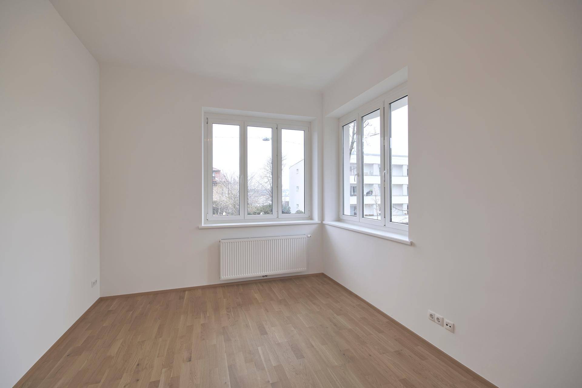Heller, leerer Raum mit hellem Holzfußboden und großen Fenstern, ideal als Wohn- oder Schlafzimmer.
