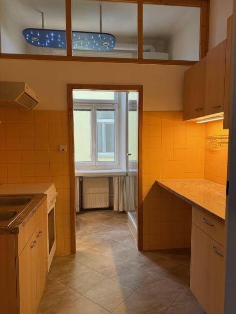 Küche mit gelben Fliesen, Holzschränken und einem Fenster, das in ein weiteres Zimmer blickt.