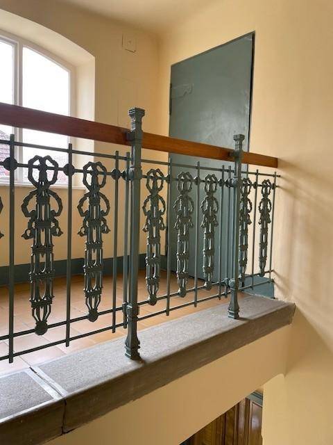 Treppenabsatz mit kunstvollem Geländer, einem großen Fenster und einer Tür in hellem Ambiente.