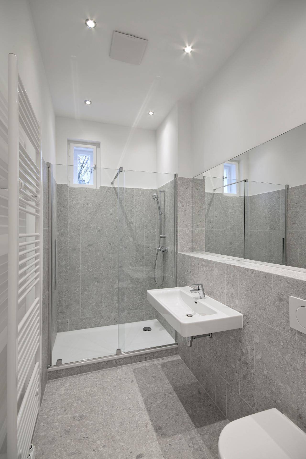 Modernes Badezimmer mit grauen Fliesen, einer ebenerdigen Dusche und einem beheizten Handtuchhalter.