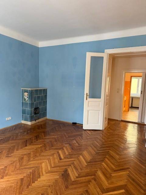 Geräumiges Wohnzimmer mit Fischgrätparkett, blauen Wänden und einem traditionellen Kachelofen.