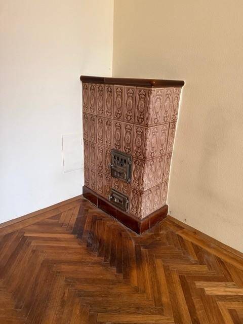 Traditioneller Kachelofen in einem Zimmer mit Fischgrätparkett und beigen Wänden.