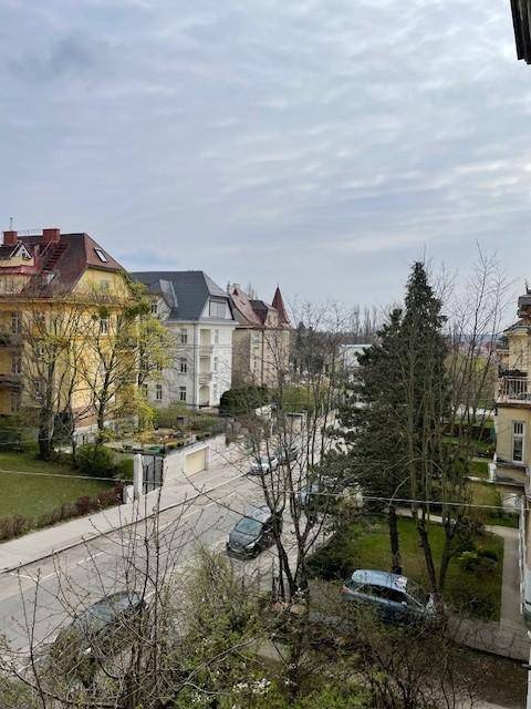 Blick auf eine Wohnstraße mit parkenden Autos und historischen Gebäuden unter einem bewölkten Himmel.
