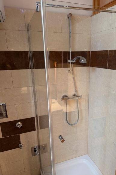 Duschbereich mit Glasabtrennung und beigefarbenen Fliesen in einem Badezimmer.